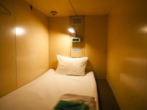 東京にあるカプセルホテルブロックルームのベッド1台と枕が備わる小さな客室です。
