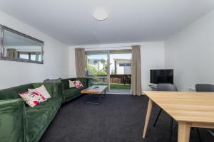 a living room with a green couch and a table at Resort-Style 2BR Alpine Apt | Pool, Spa & Garage in Wanaka