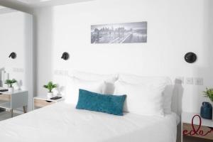 a white bedroom with a white bed with a blue pillow at דירת חדר שינה וסלון עם מרפסת ליד הים - By Edomlux in Eilat