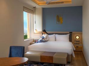 a woman sitting on a bed in a room with a window at O by Tamara Coimbatore in Coimbatore