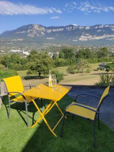 una mesa amarilla y dos sillas con montañas en el fondo en Appartement duplex indépendant, dans maison., en Tresserves