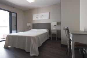 a white bedroom with a bed and a table and a desk at Hostal Emeritae in Mérida