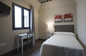 a bedroom with a bed and a desk and a window at Hostal Emeritae in Mérida