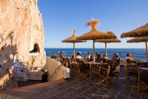 people sitting at tables with straw umbrellas on the beach at Villa Maria Del Mar by Villa Plus in Cala'n Porter