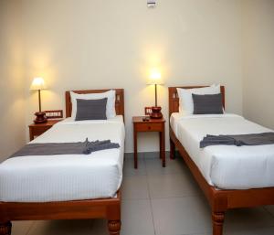 two beds in a room with two lamps on tables at Mango Hill La Serene Puducherry in Pūrnānkuppam