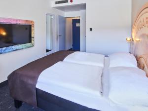 a bedroom with a large white bed with a flat screen tv at B&B Hotel Offenbach-Kaiserlei in Offenbach