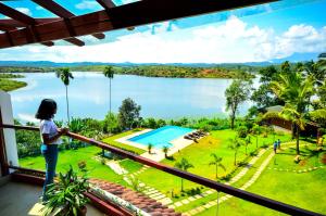 a woman standing on a balcony looking out at a lake at LakeRose Wayanad Resort in Ambalavayal