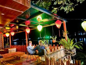 2 hommes assis sur des chaises sous une terrasse éclairée dans l'établissement Phong Nha Coco House, à Phong Nha