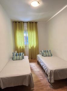 two beds in a room with yellow curtains at GranVia Fira Apartment in Hospitalet de Llobregat
