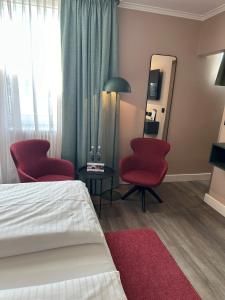 ミュンヘンにあるHotel Metropol by Maier Privathotelsの赤い椅子2脚と鏡が備わるホテルルームです。