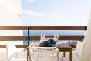 a wooden table with glasses and chairs on a balcony at Home2Book Stylish Studio Ocean View Tabaiba in Tabaiba