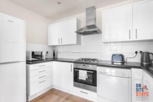 eine Küche mit weißen Schränken und einem Herd mit Backofen in der Unterkunft OnSiteStays - Cosy 2-Bedroom Apartment with Free Parking, Wi-Fi & London Links in Northfleet