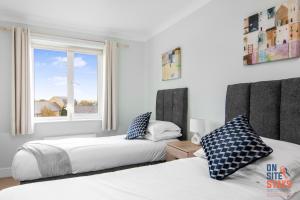 two beds in a bedroom with a window at OnSiteStays - Cosy 2-Bedroom Apartment with Free Parking, Wi-Fi & London Links in Northfleet