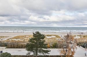 uma praia com pessoas andando na areia e no oceano em Baltic Hideaways Beach Hotel Warnemünde em Warnemünde
