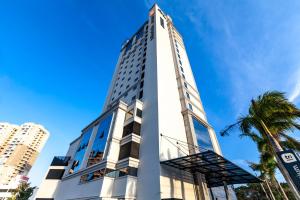 a tall white building with a palm tree at Tri Hotel Premium Itapema in Itapema