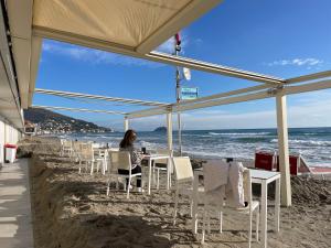 a woman sitting at a table on the beach at Locanda Kon Tiki in Alassio