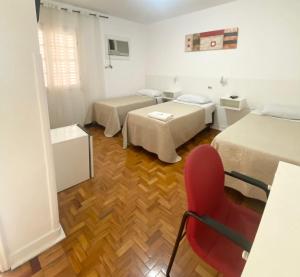a room with two beds and a red chair at Hotel Cidade De Bauru in Bauru