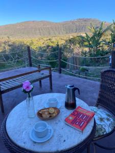 una mesa con una tetera y un jarrón de flores y un libro en Casa Raízes Capão en Vale do Capao