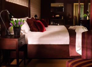 a bedroom with a bed with white sheets and red pillows at Stoke Place- Part of the Cairn Collection in Slough