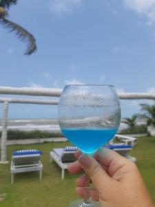 una mano che tiene un bicchiere di vino con una spiaggia dentro di A 2 passos do paraíso a Rio Tinto