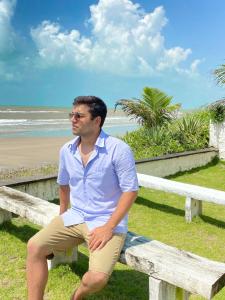 un hombre sentado en un banco cerca de la playa en A 2 passos do paraíso en 