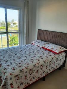 uma cama com um edredão floral num quarto com uma janela em Condomínio Cordeiro em Arroio do Sal