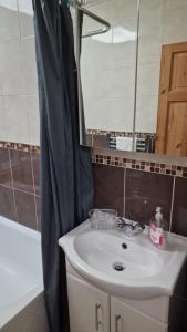 een badkamer met een wastafel, een spiegel en een bad bij Comfortable 2 bedroom house with free parking and great transport links in Dagenham