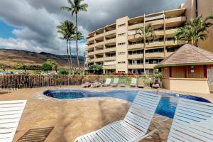 a swimming pool with two chairs and a building at Island Sands Resort Condominiums in Wailuku