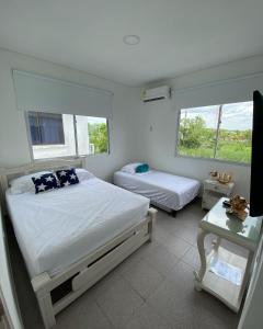 1 dormitorio con 2 camas, mesa y 2 ventanas en Cabaña Arrecife 07, en Coveñas