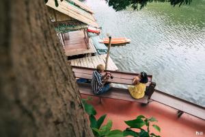 duas pessoas sentadas num banco ao lado da água em ชอว์ งาทอง รีสอร์ต Chor Ngar Thong Erawan em Kanchanaburi