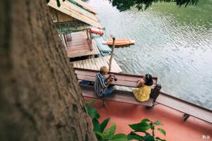 two people sitting on a bench next to the water at ชอว์ งาทอง รีสอร์ต Chor Ngar Thong Erawan in Kanchanaburi City