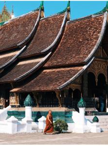 a monk walking in front of a large building at Thavixay Hotel in Vientiane