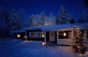 a house with a christmas tree in the snow at night at Kuurala apartment in Rovaniemi
