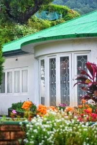 una casa blanca con techo verde y algunas flores en Waterfield Bungalow by Liyozi Leasiure, en Nuwara Eliya