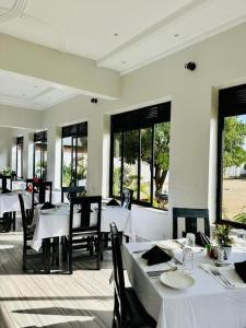 un restaurante con mesas y sillas blancas y ventanas en Kacoke Madit Hotel and Cultural Centre, Gulu en Gulu