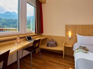 una camera d'albergo con scrivania, letto e finestra di ibis Luzern Kriens a Lucerna