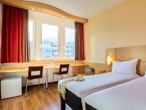 um quarto de hotel com duas camas e uma secretária em ibis Luzern Kriens em Lucerna