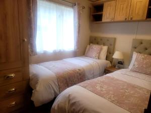 two beds in a bedroom with a window at New Forest 2-Bed Premium Holiday Home, Hoburne Bashley Holiday Park, New Milton in New Milton