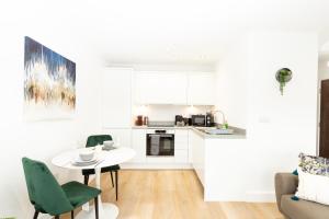 a white kitchen with a table and green chairs at Stylish Studio Apt overlooking Old Trafford in Manchester