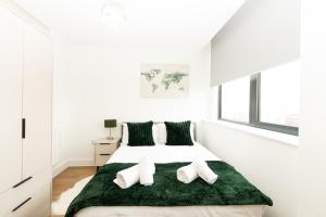 a white bedroom with a large bed with green blanket at Stylish Studio Apt overlooking Old Trafford in Manchester