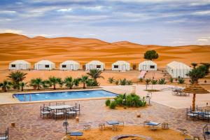 ein Resort in der Wüste mit einem Pool, Tischen und Stühlen in der Unterkunft Yakout Merzouga Luxury Camp in Merzouga