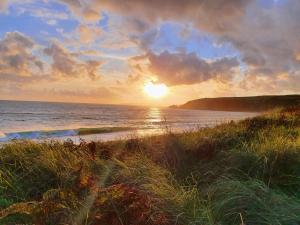 a sunset on a beach with the ocean and grass at Primrose Cottage in Helston