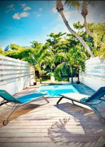 une piscine avec deux chaises et des palmiers dans l'établissement *Secret Sand* Cheerfull Town beach house villa, à La Baie-Orientale