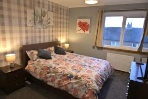 a bedroom with a bed with a comforter and two windows at Take A Break and Unwind At This Peaceful Home in Saltcoats