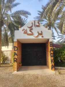 a building with a sign on it with palm trees at Dar Barka in Kebili
