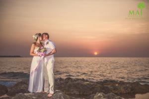 a bride and groom kissing on the beach at sunset at 普吉岛-迈考海滩水疗度假村PL- Maikhaolak Beach Village in Khao Lak