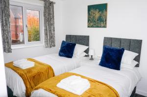 two beds in a white room with blue pillows at The Oasis in Wigan