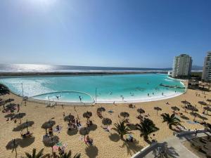 a large swimming pool on a beach with people and umbrellas at Departamento La Serena Laguna del Mar in La Serena