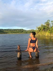 a woman sitting on a bench in the water with a teddy bear at EcoMar - Pousada de Experiência in Barra de São Miguel