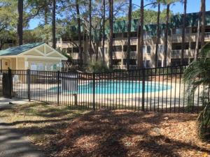 a fence with a pool in front of a building at Peaceful Treetop Condo - 2br/2ba in Hilton Head Island